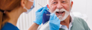 Doctor checking up patient's teeth at dentist office; senior man at dental checkup